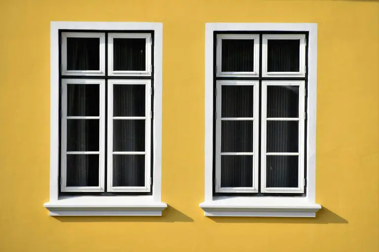 Two white-framed windows on yellow wall.