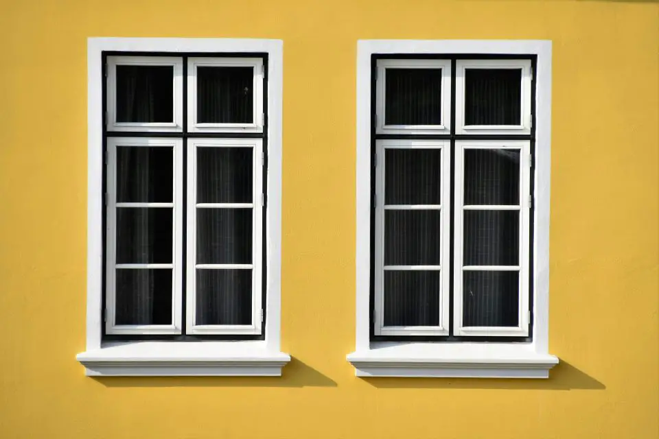Two white-framed windows on yellow wall.