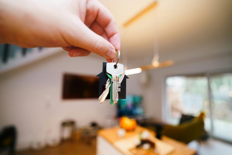 Hand holding house keys in bright living room.