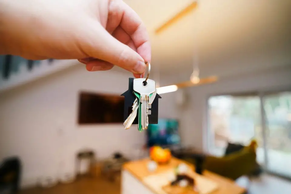 Hand holding house keys in bright living room.