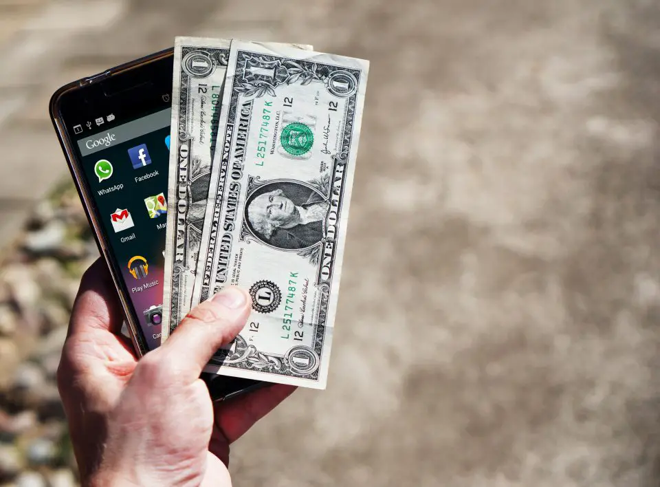 Hand holding mobile phone and US dollar bills.