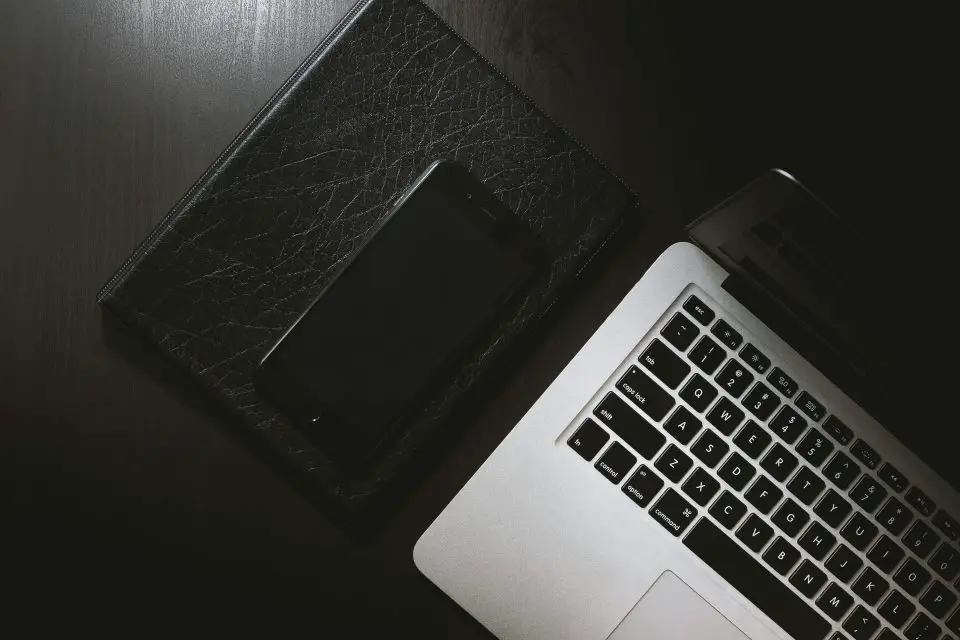 Laptop, smartphone, leather notebook on dark desk.
