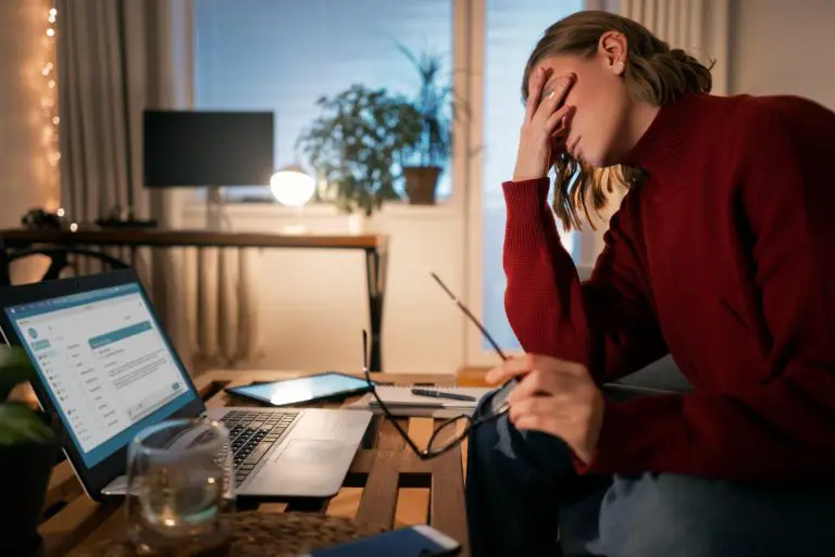 Woman stressed at laptop, holding head with hand.