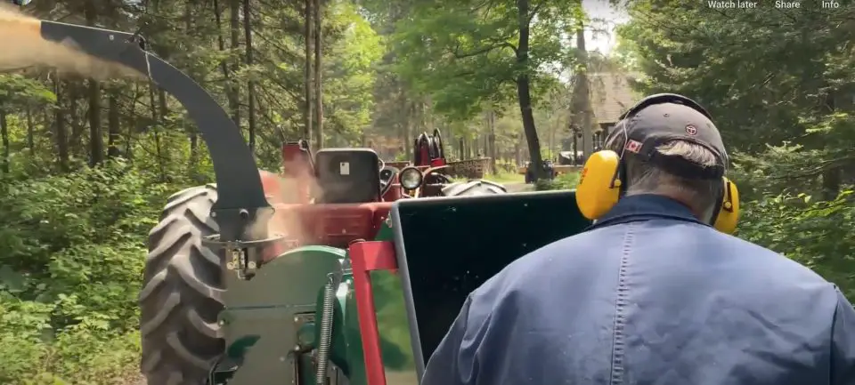 Person using wood chipper in forested area.