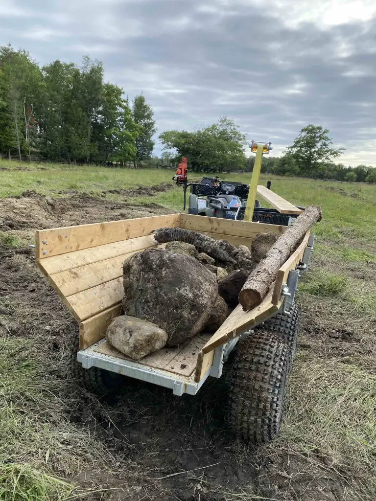 ATV with trailer carrying rocks and logs.