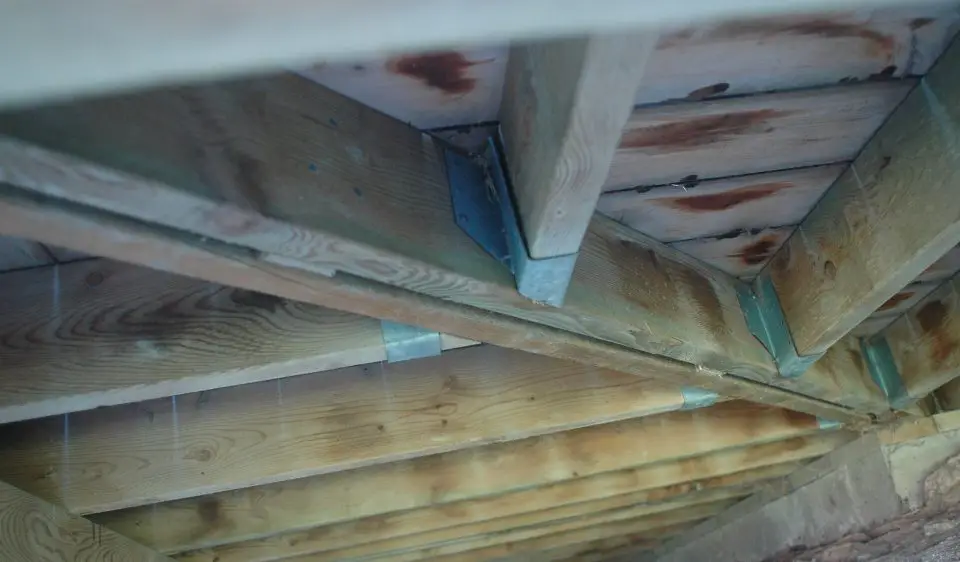 Wooden floor joists with metal brackets in basement.