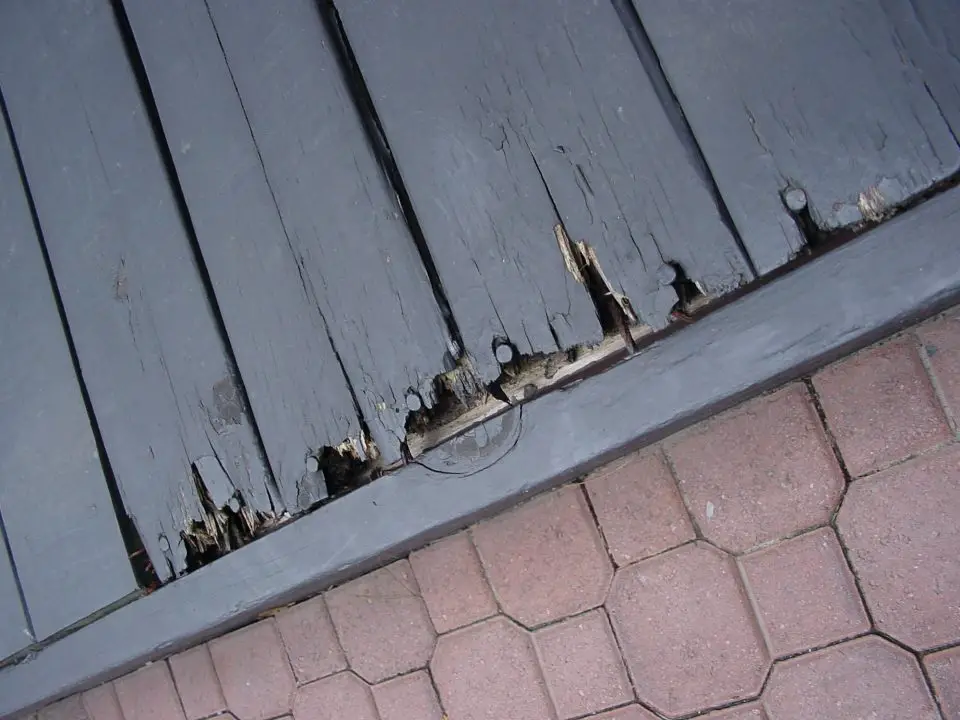 Damaged wooden deck beside brick pavement.