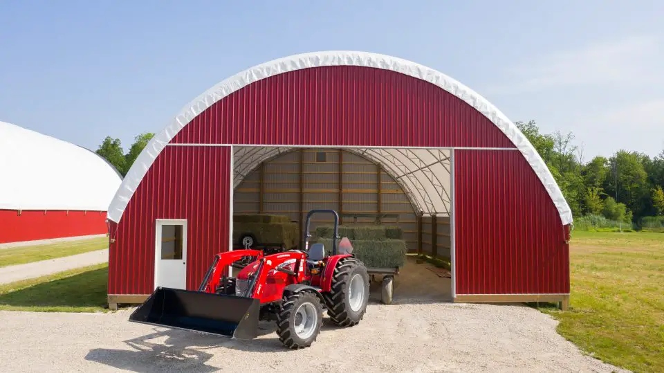 Red tractor parked outside red barn.