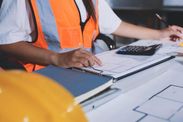 Engineer reviewing plans at desk with calculator.