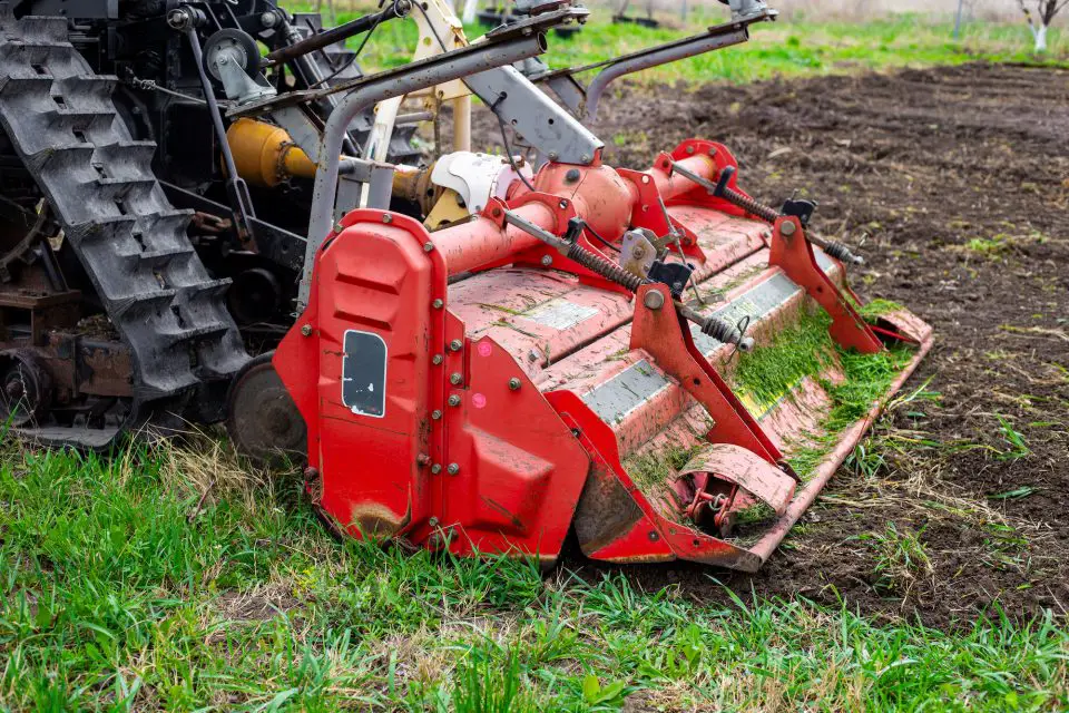 Red rotary tiller on grassy field