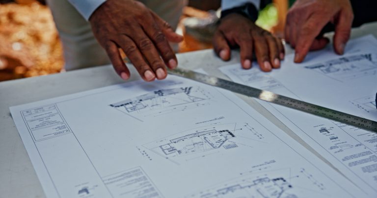 Hands reviewing architectural blueprints with ruler.